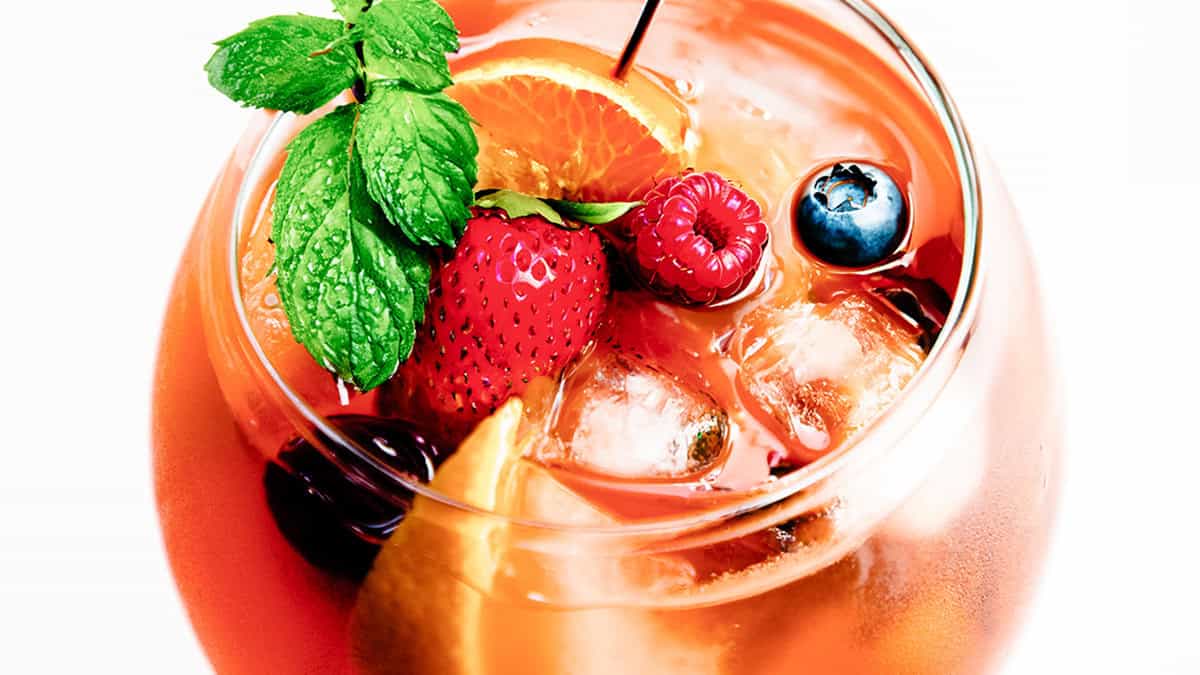 A close up image of a glass of Rosé Sangria with fresh fruit, mint and a cocktail stick in the glass.