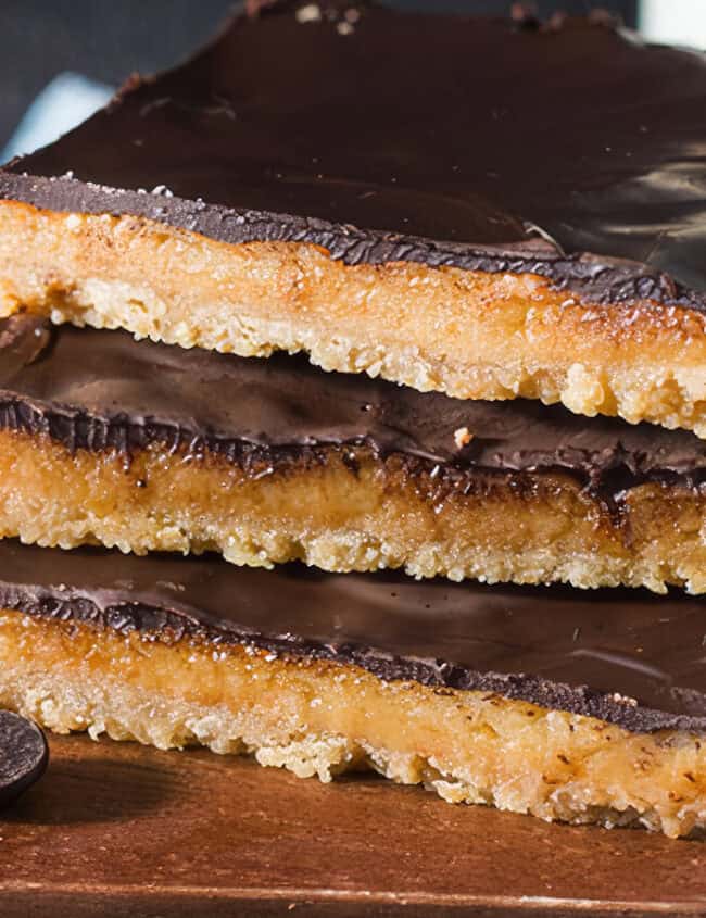 Three Salted Toffee Cookie Bars stacked on a wooden board.