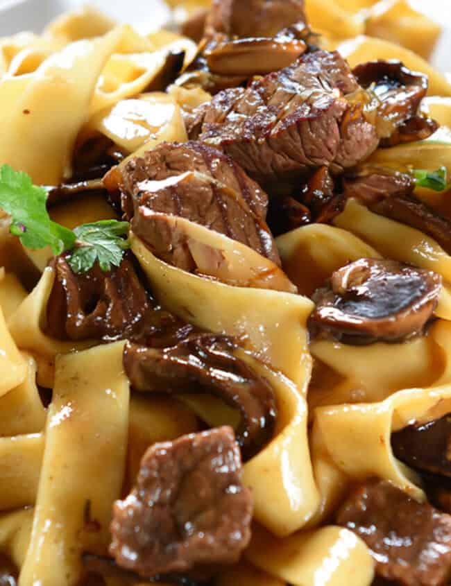 A close up image of a bowl filled with Beef with Mushrooms and noodles.