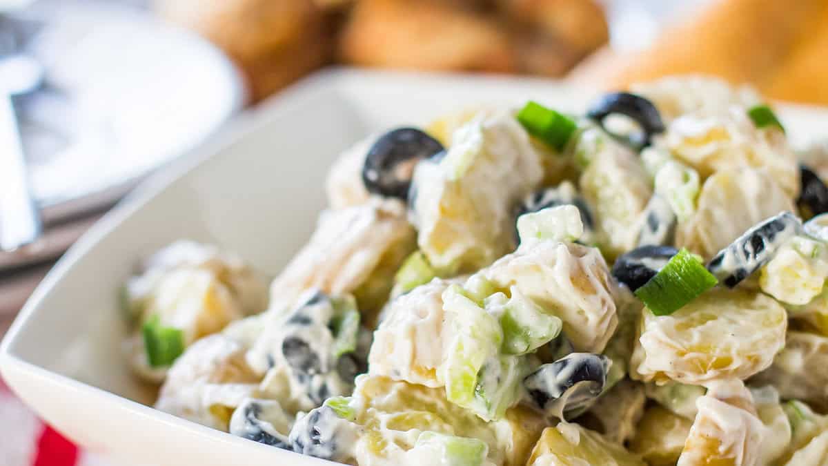 a bowl of potato salad with chicken in the background.