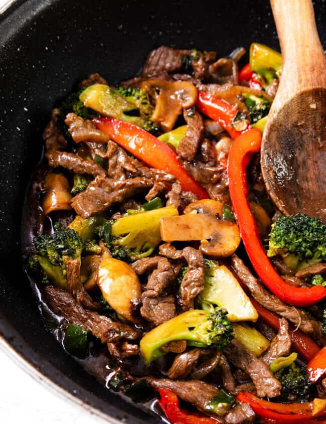 A colorful steak stir fry in a black skillet, featuring thinly sliced beef mixed with broccoli, bell peppers, and mushrooms.