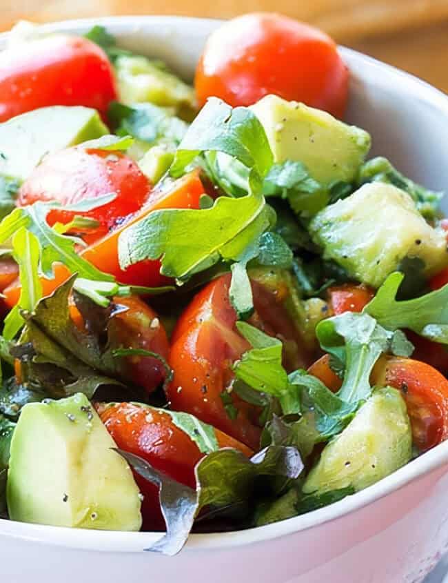 A bowl of bright and colorful tomato avocado salad with some bread in the background.