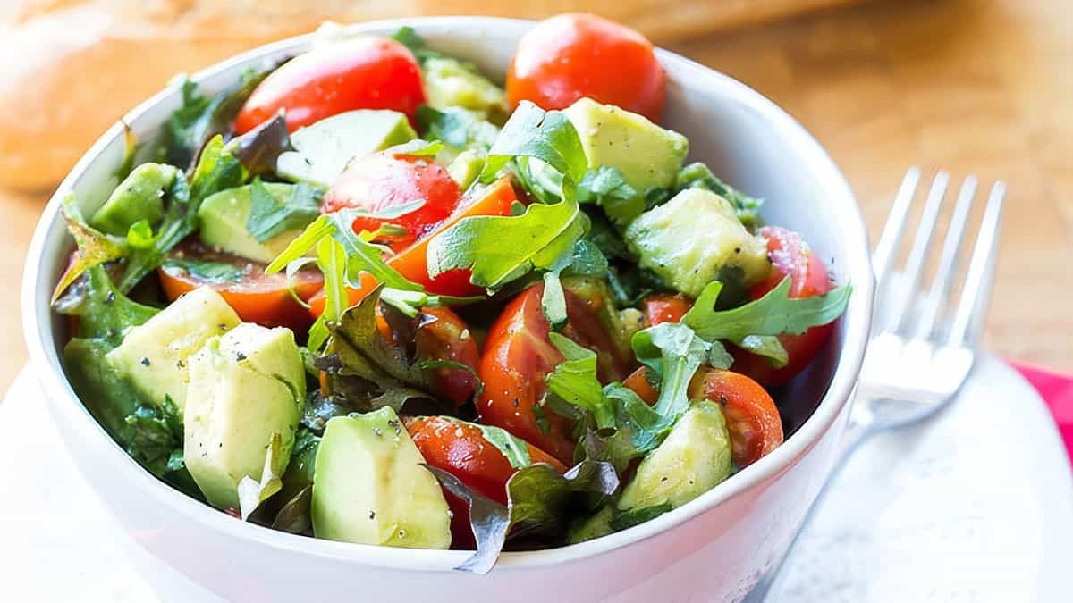 A bowl of bright and colorful tomato avocado salad with some bread in the background.