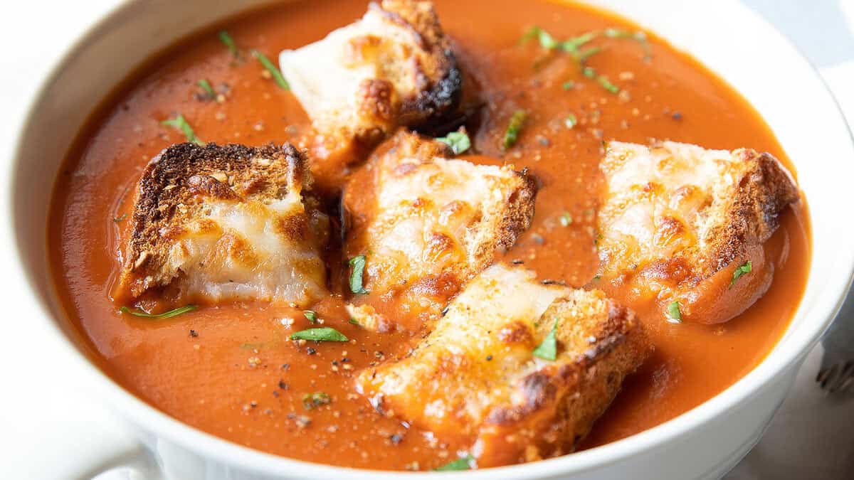 A close up image of Tomato Soup topped with Cheesy Croutons on top.