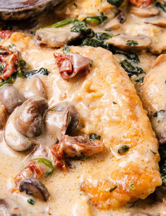 A close up image of a pan of Creamy Tuscan Chicken with mushrooms, spinach and sundried tomatoes.