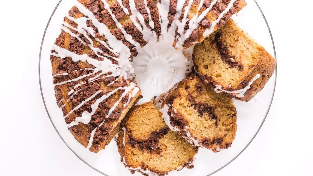 A Chocolate Coffee Cake with white icing on a glass cake stand.