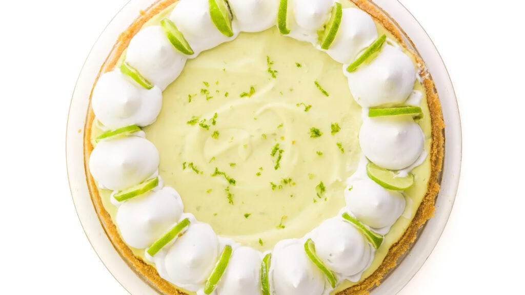 A close up image of a Dairy-Free Key Lime Pie piped with white whipped topping.