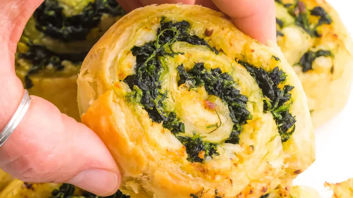 Close-up of vegan spinach cheese pinwheel held in fingers