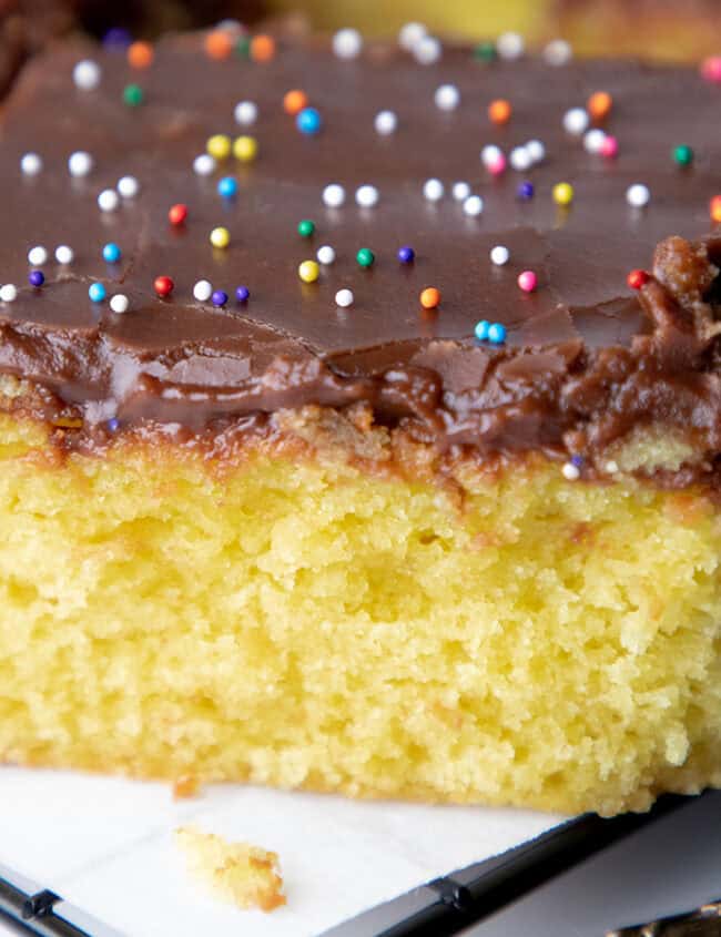 A close up image of a slice of yellow cake with chocolate frosting.