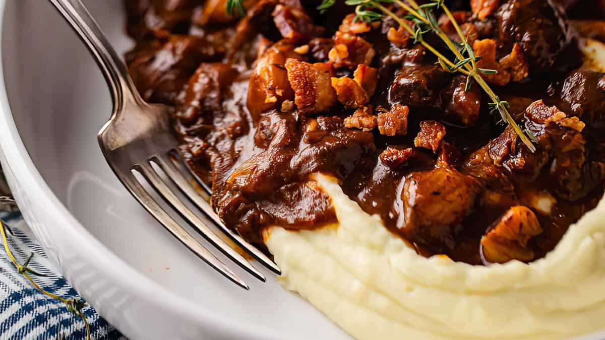 A white plate with mashed potatoes and beef bourguignon.