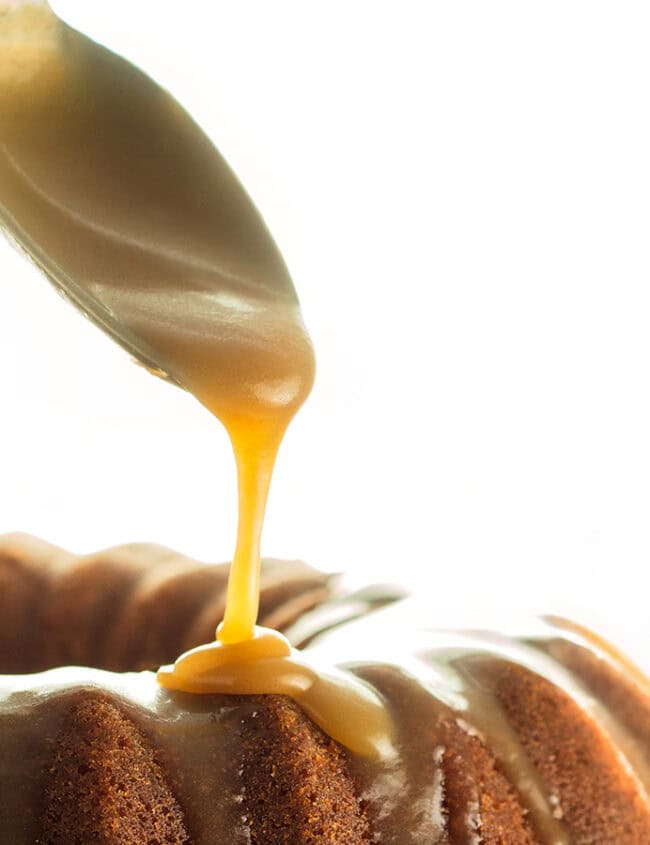 A spoon adding caramel glaze to a cake.