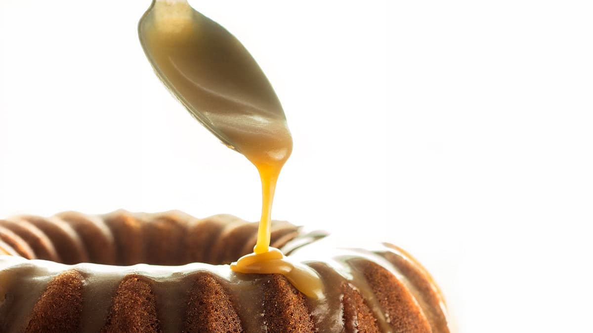 A spoon adding caramel glaze to a cake.