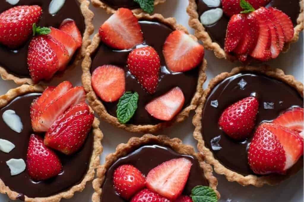 A close up image of Chocolate Strawberry Tartlets with shiny chocolate filling topped with strawberries.