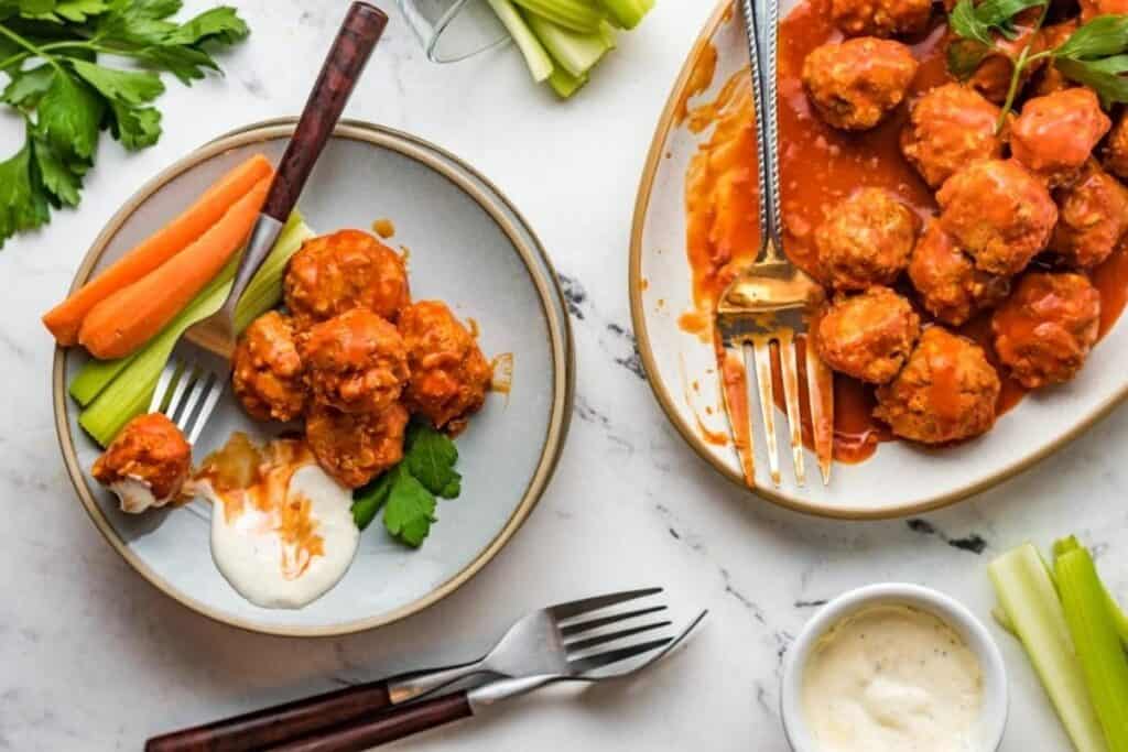 Twp plates of Slow Cooker Buffalo Chicken Meatballs with forks.