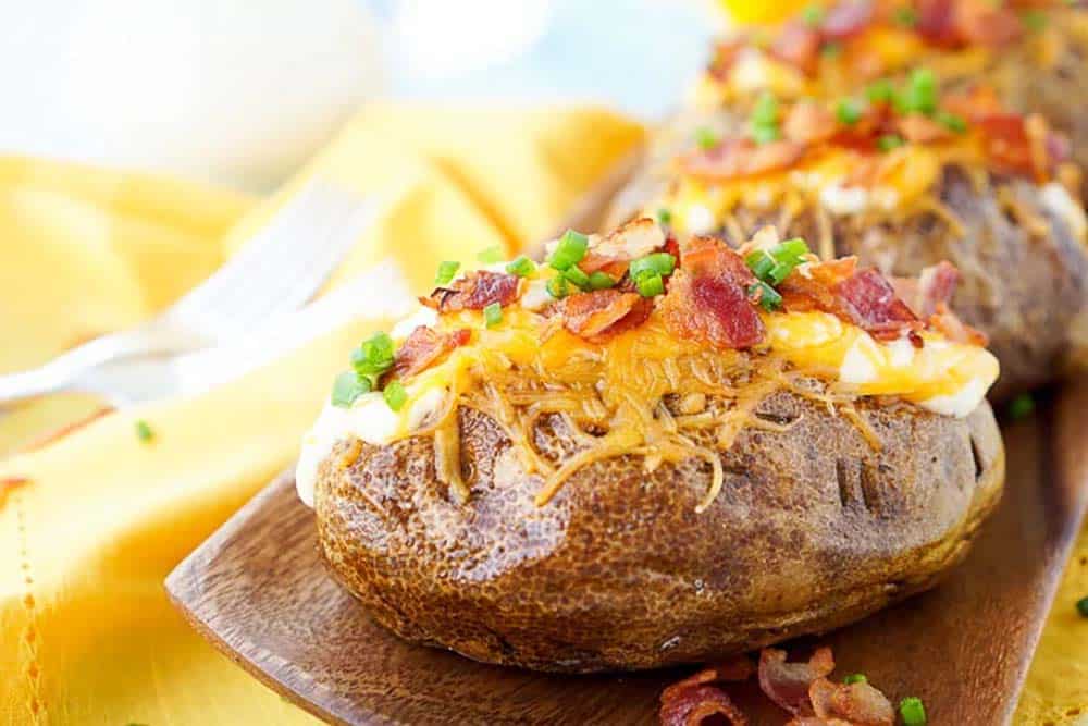 A loaded baked potato on a plate with more in the background.