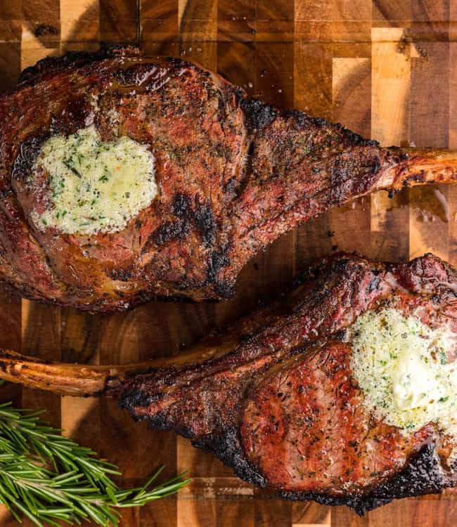 Two Smoked Tomahawk Steaks topped with herbs and butter.