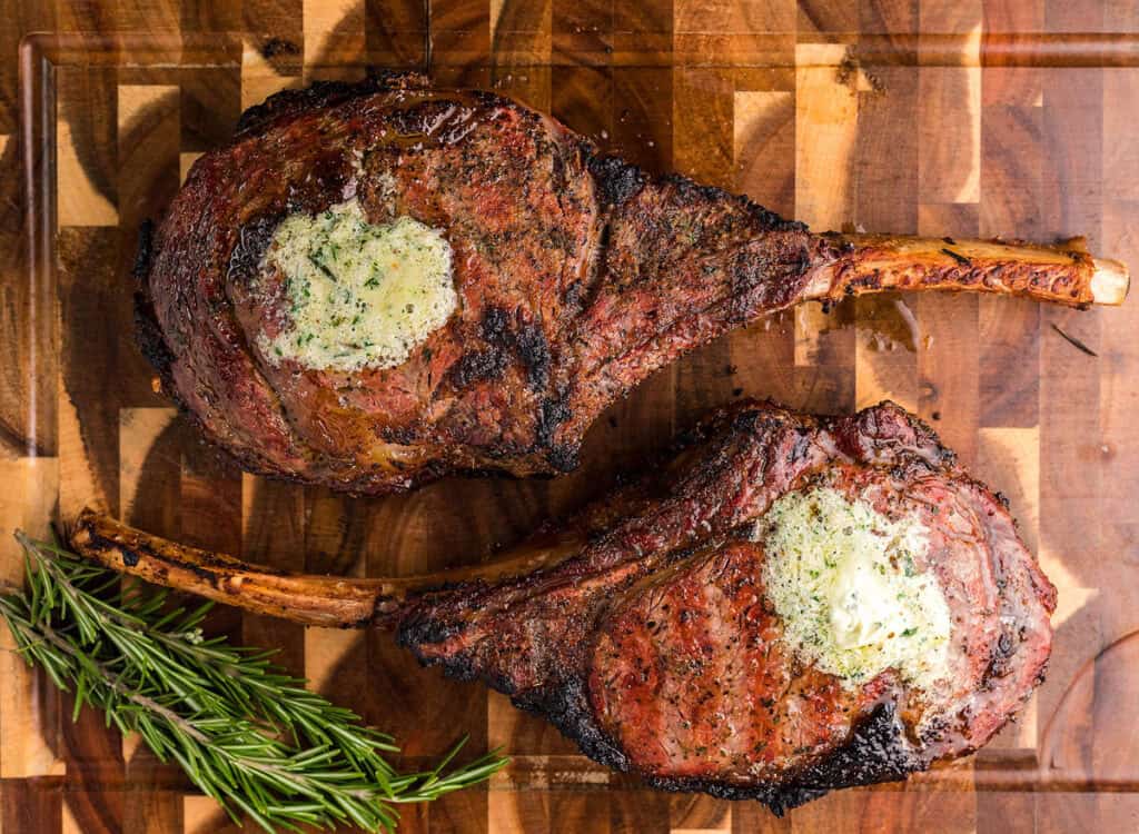 Two Smoked Tomahawk Steaks topped with herbs and butter.