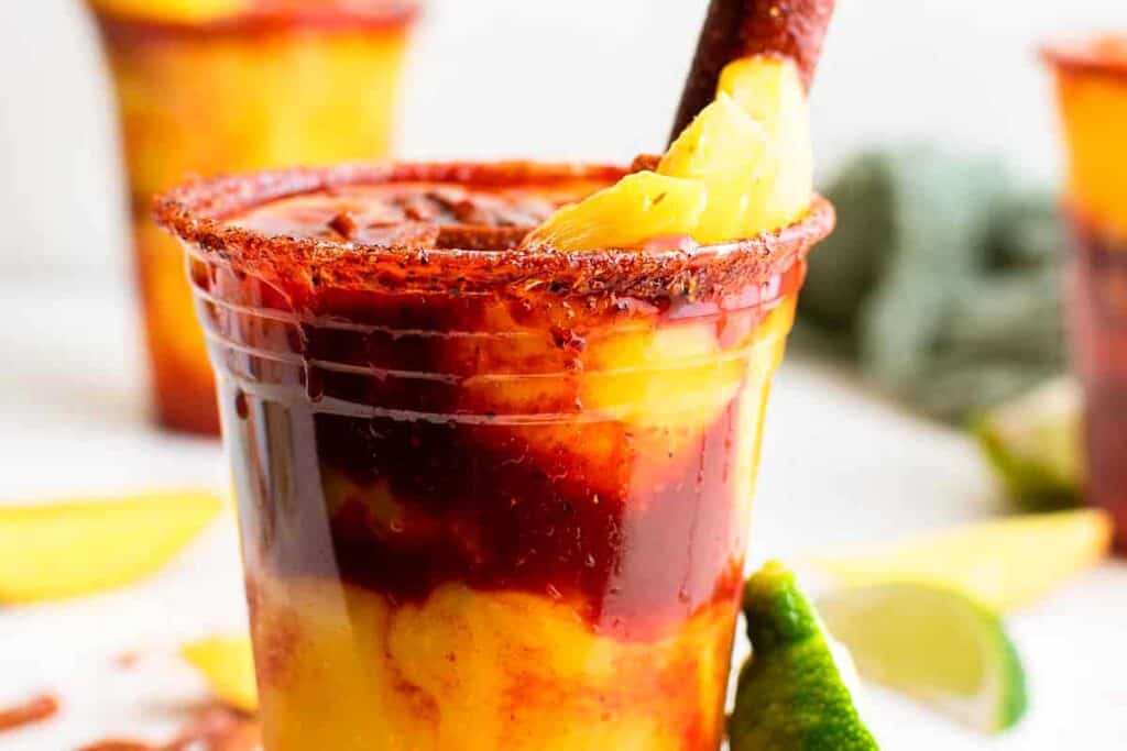 A colorful Mangonadas Rin a clear glass with fruit.