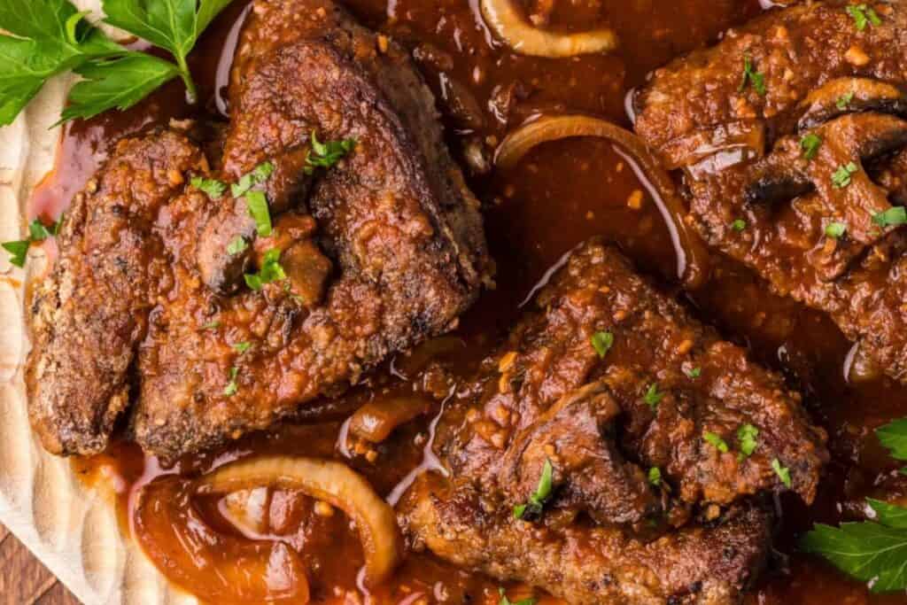 A plate full of Round Steak In The Oven with sauce, onions and mushrooms.