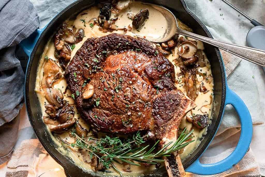 A pan of a Pan Seared Steak and Mushrooms garnished with rosemary.