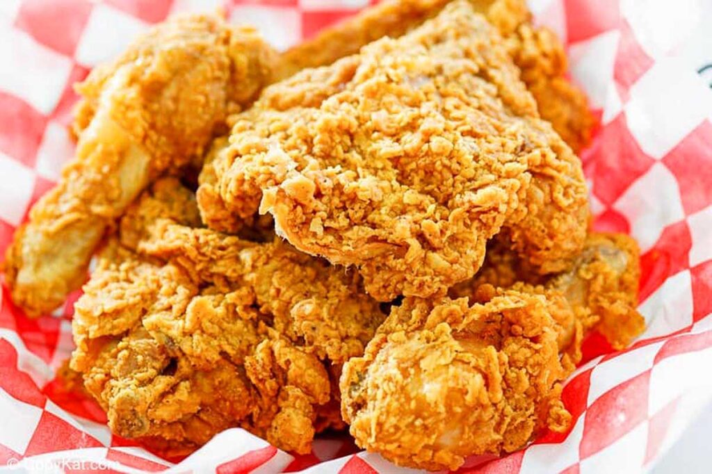 A basket of golden brown fried chicken on a red and white checkered napkin.