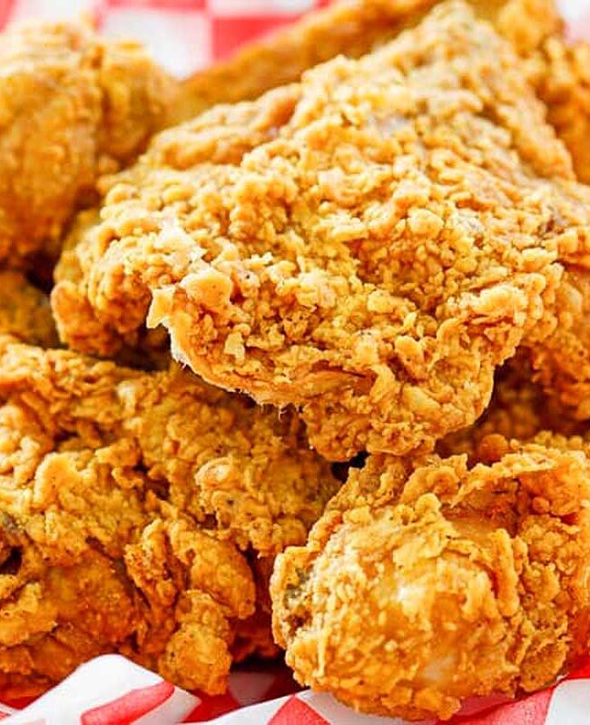 A basket of golden brown fried chicken on a red and white checkered napkin.