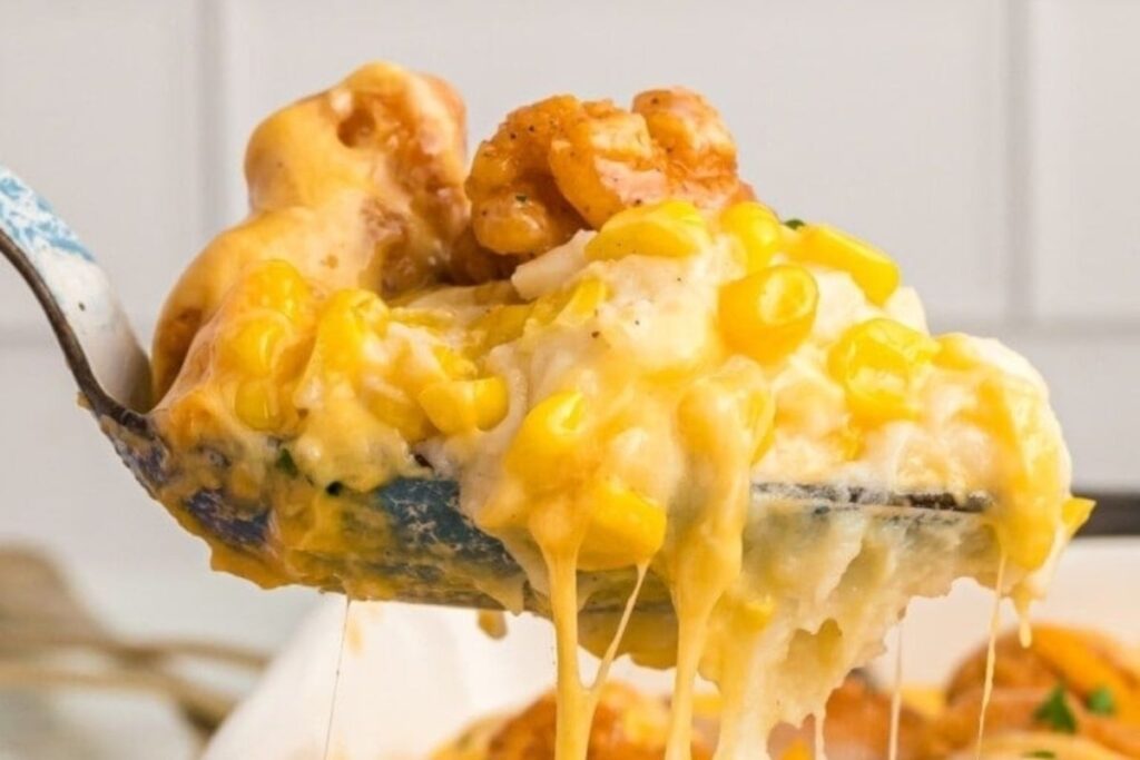 Close-up of a spoon with a scoop of casserole with cheese, chicken and corn.