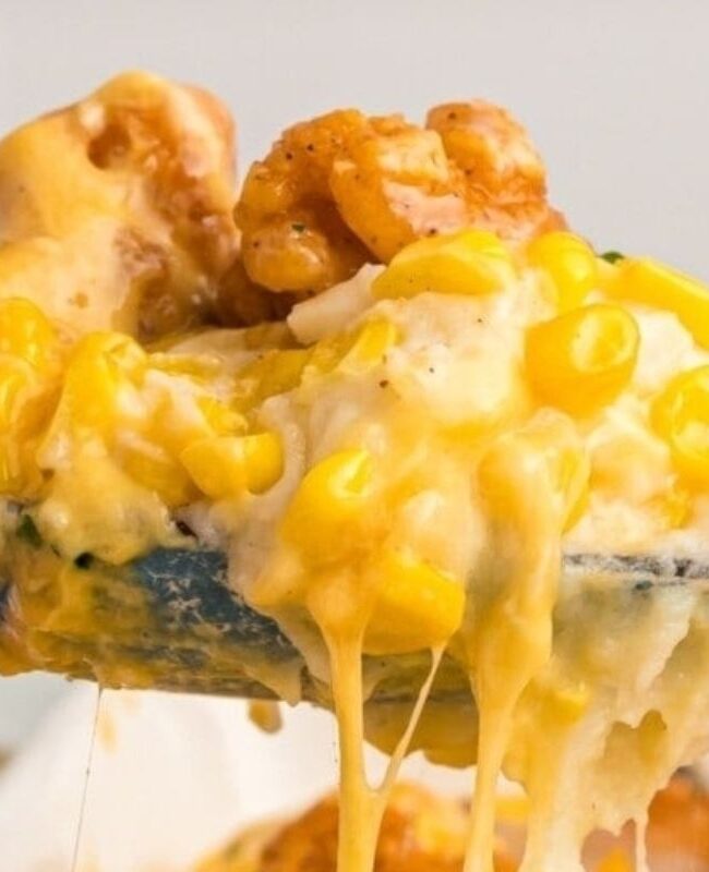 Close-up of a spoon with a scoop of casserole with cheese, chicken and corn.