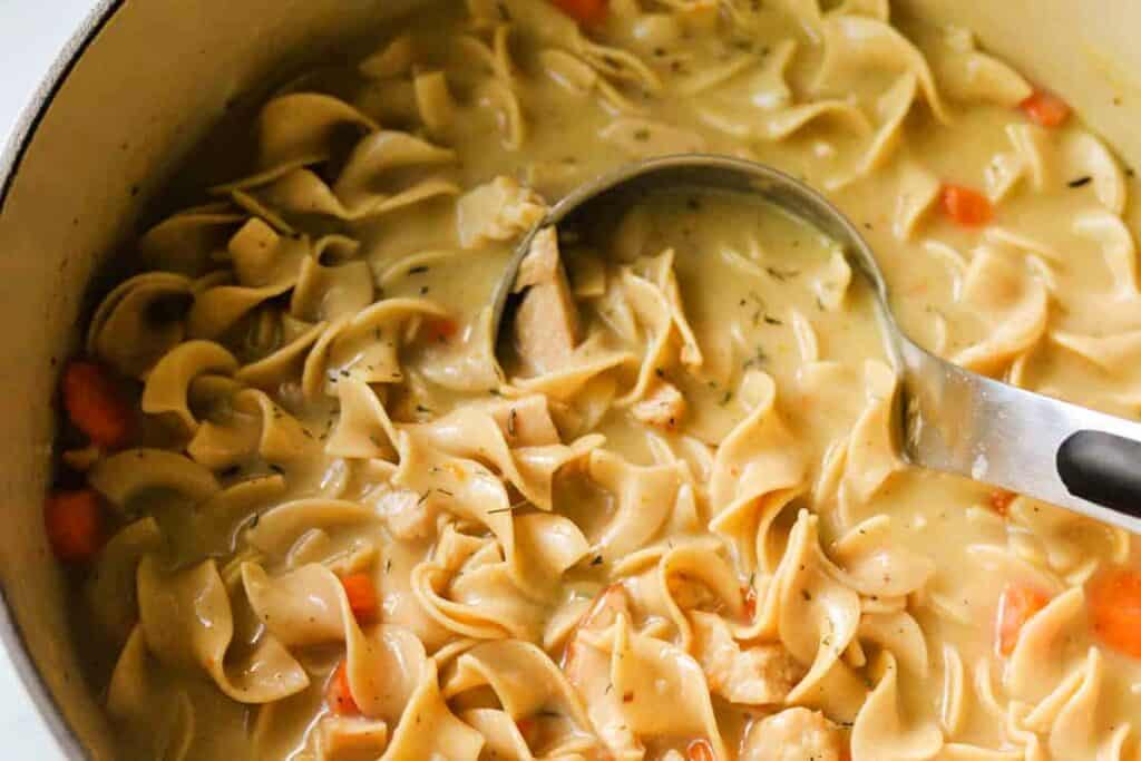 A pot of chicken noodle soup with a ladle resting on the rim.