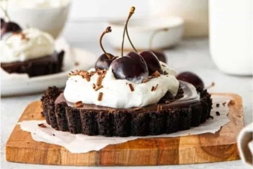 A Chocolate Ganache Tart topped with whipped cream and cherries.