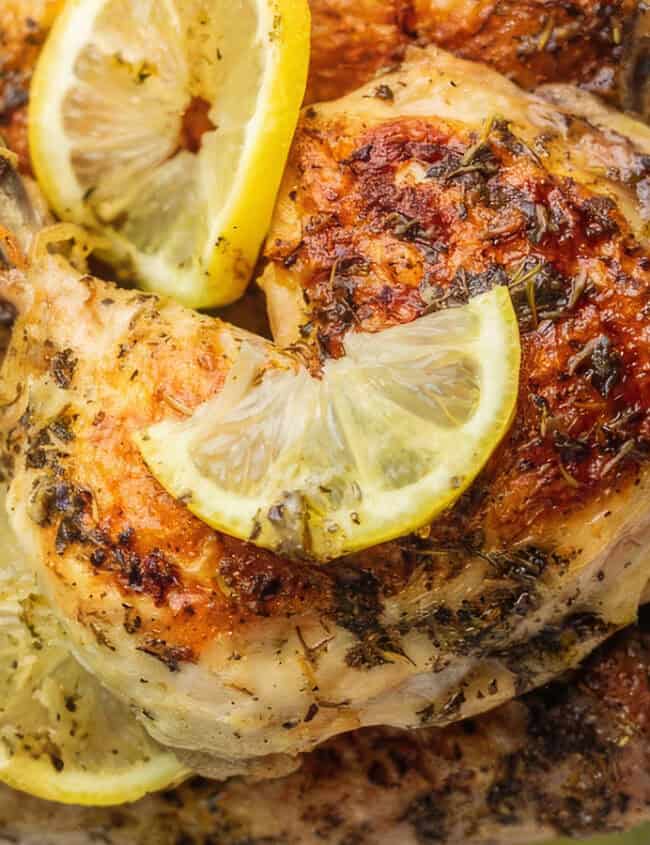 A close up image of a platter of chicken legs garnished with lemon slices.