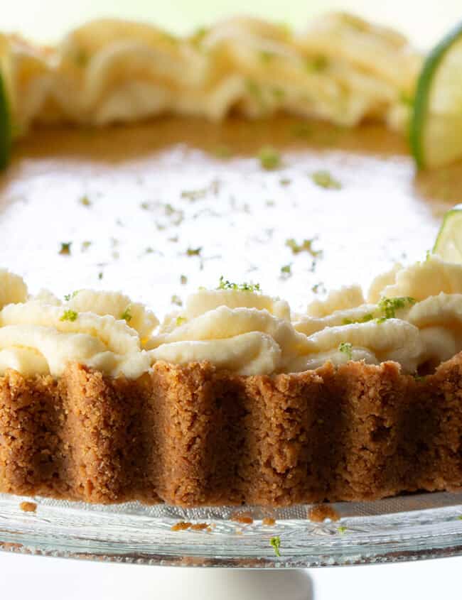 A key lime pie swirled with whipped cream around the edge and garnished with lime slices and zest.