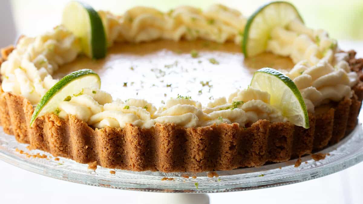 A key lime pie swirled with whipped cream around the edge and garnished with lime slices and zest.