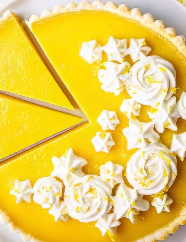 A sliced lemon tart with whipped cream and lemon slices on a white plate.