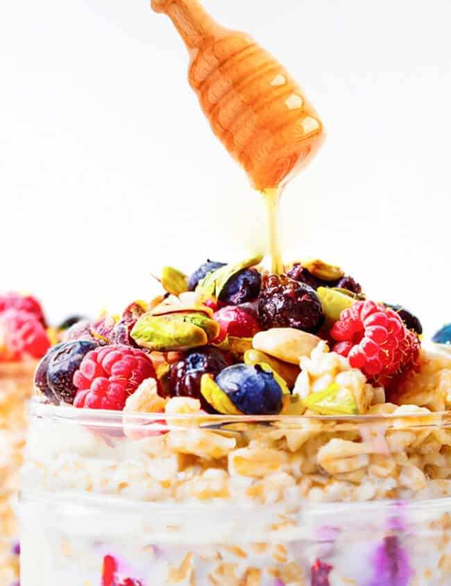 Drizzling honey from a honey dipper over overnight oatmeal in a jar.