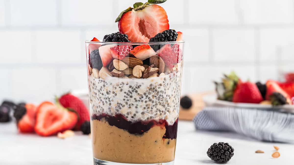 a glass of layered PBJ Overnight Oats in a glass topped with berries.