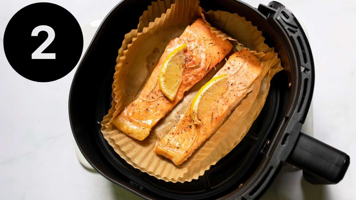 two salmon fillets in an air fryer lined with baking paper.