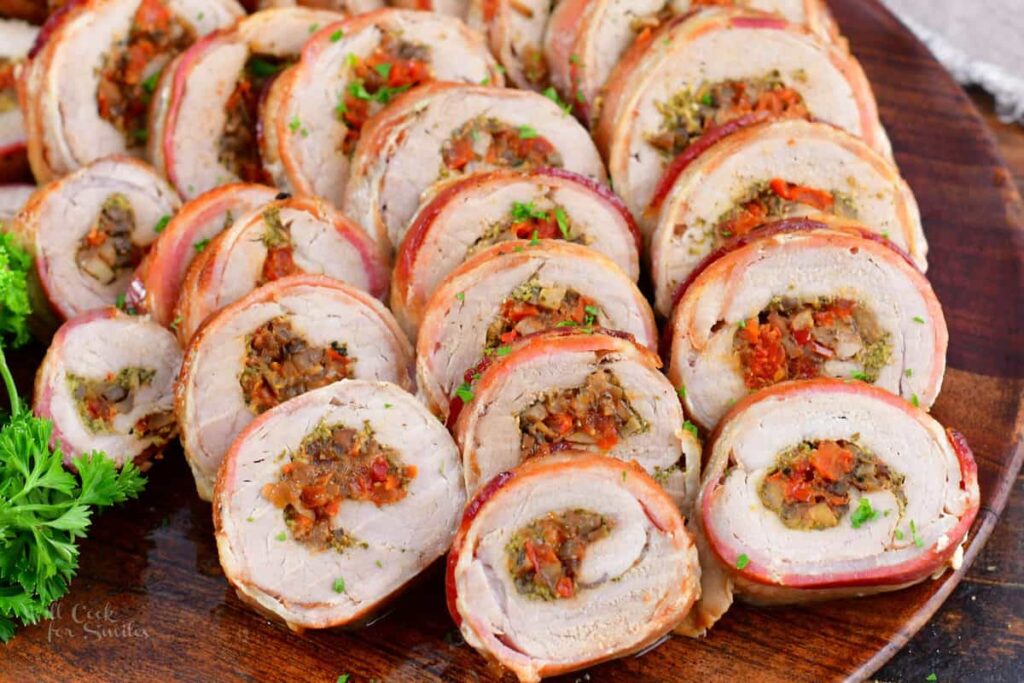 Sliced stuffed pork tenderloin spread in a large wooden platter.