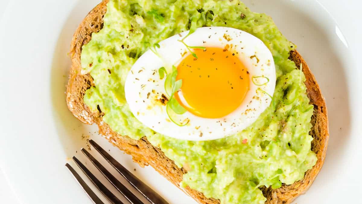 Toast with Guacamole and soft boiled egg on white tray with a fork.