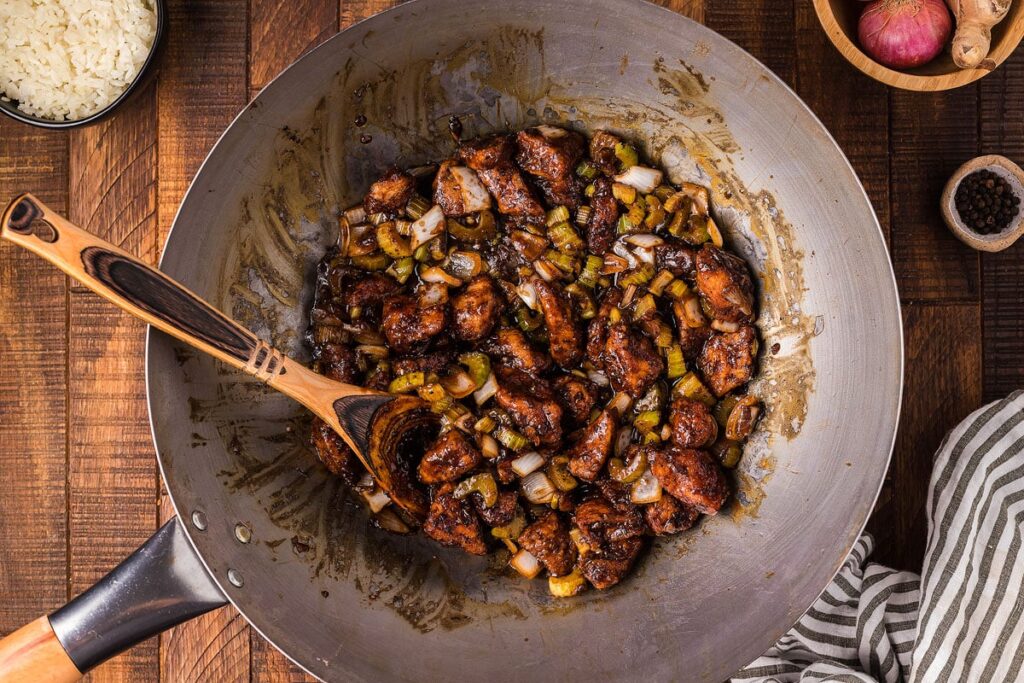 A wok with Black Pepper Chicken and a wooden spoon in it.