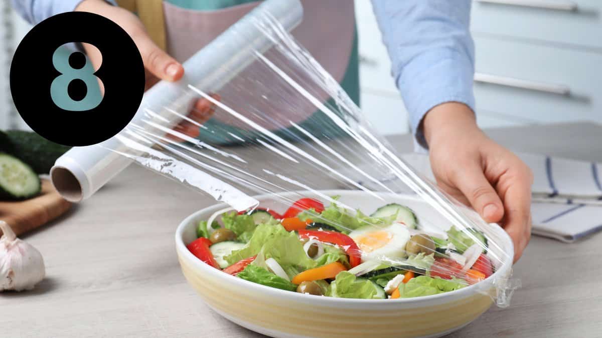 A person holding a plastic wrap over a bowl of salad.