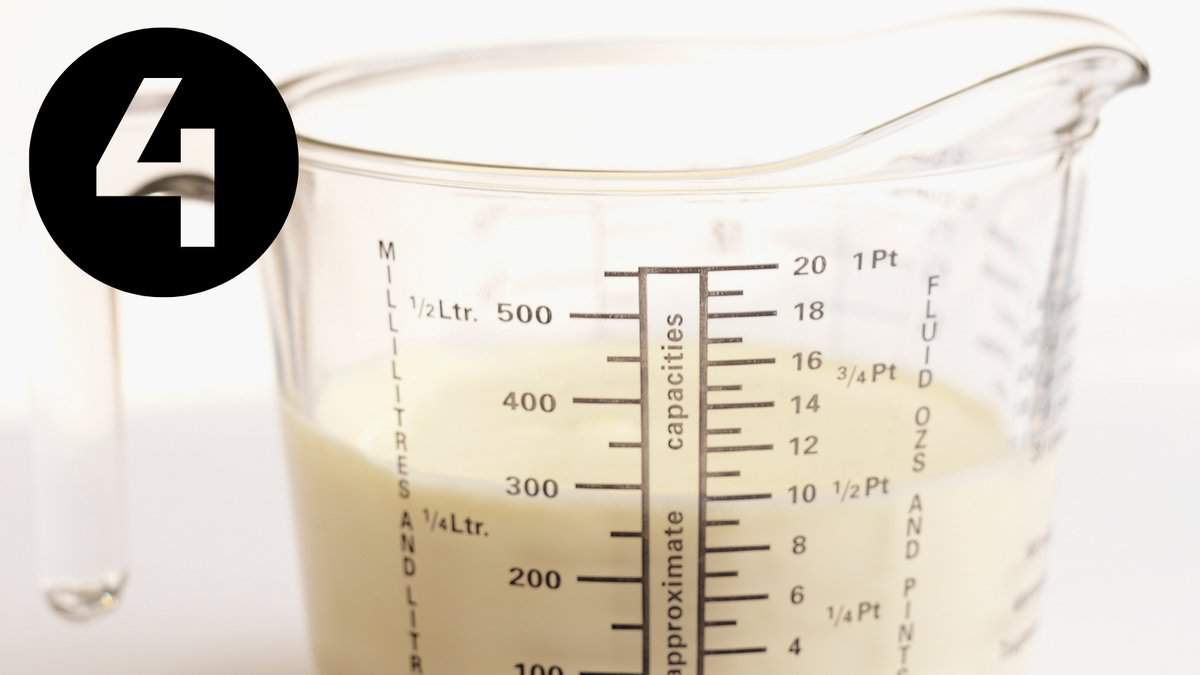 A measuring cup filled with condensed milk on a white surface.