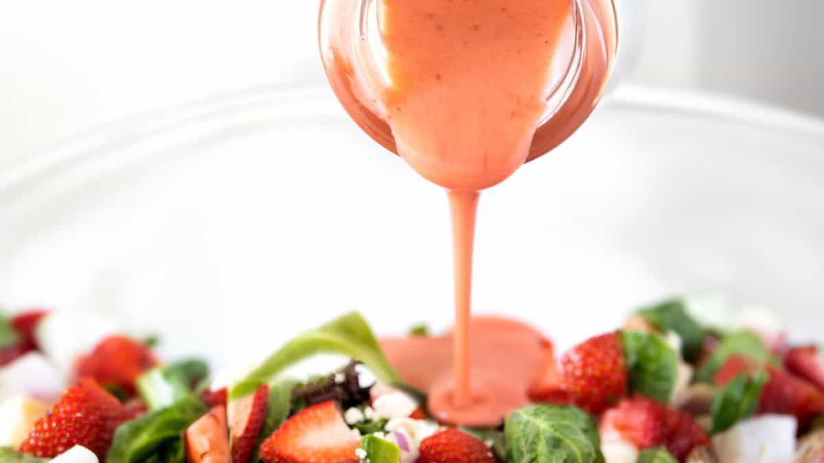 Strawberry salad dressing being poured onto a salad.