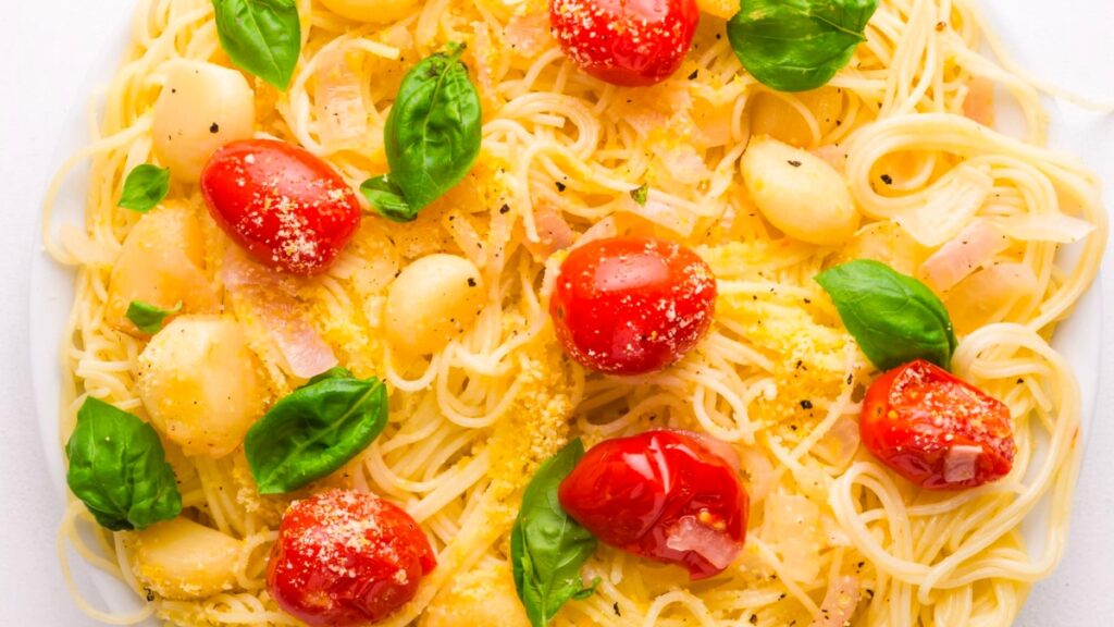 Looking down on garlic confit pasta, topped with cherry tomatoes, fresh basil leaves, and tender cooked garlic.