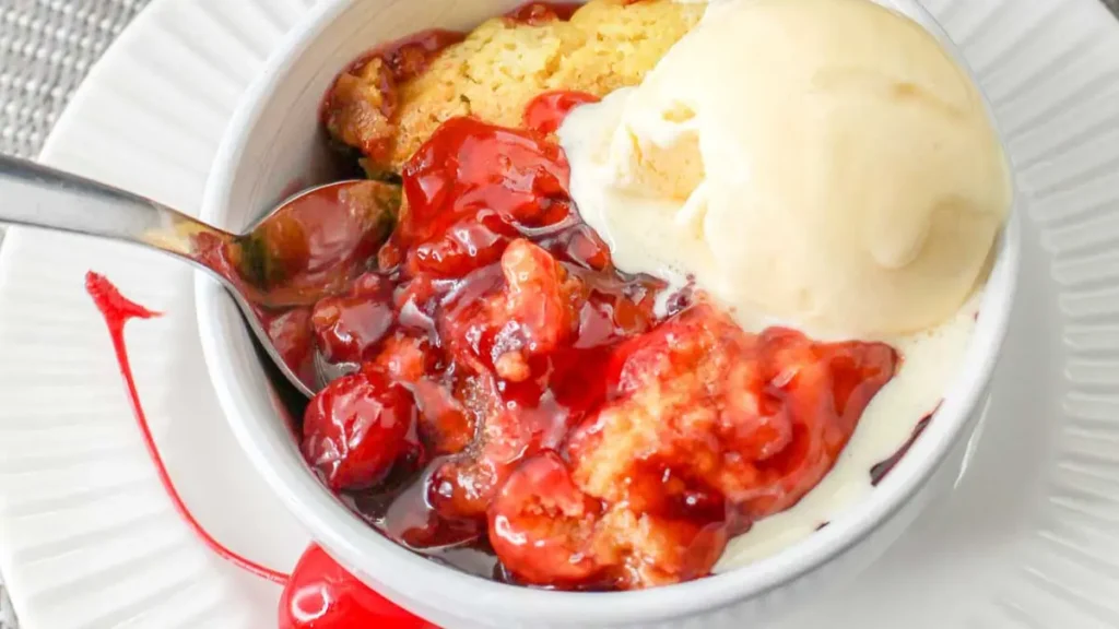 Crockpot Cherry Dump Cake in a bowl with cherry sauce and vanilla ice cream.