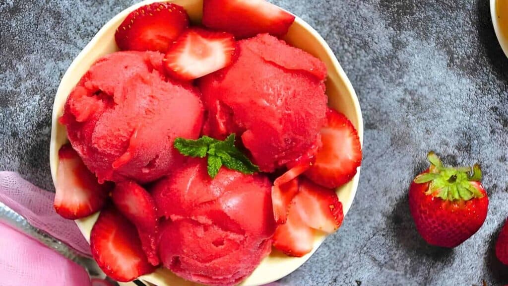 A bowl of Strawberry Sorbet garnished with fresh strawberries and mint.