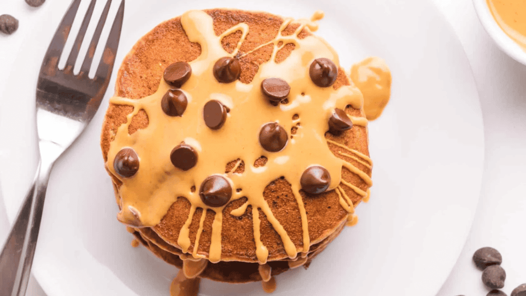 A stack of protein pancake topped with caramel sauce and chocolate chips.