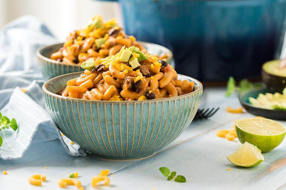 A vowl of One Pot Cheesy Taco Pasta with limes on the table.