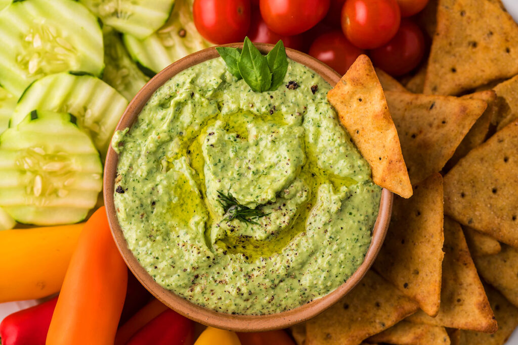 Avocado Herb Green Goddess Dip in a bowl surrounded by chips.