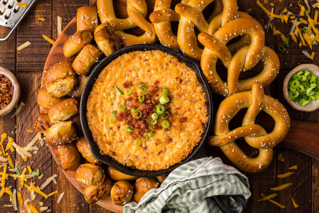 Smoked Gouda Bacon Cheddar Cheese Dip surrounded by soft pretzels on a platter.